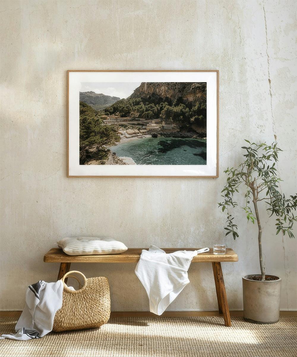 A gallery wall with a photo of a serene Mediterranean cove featuring turquoise water, wooded hills, and small buildings.