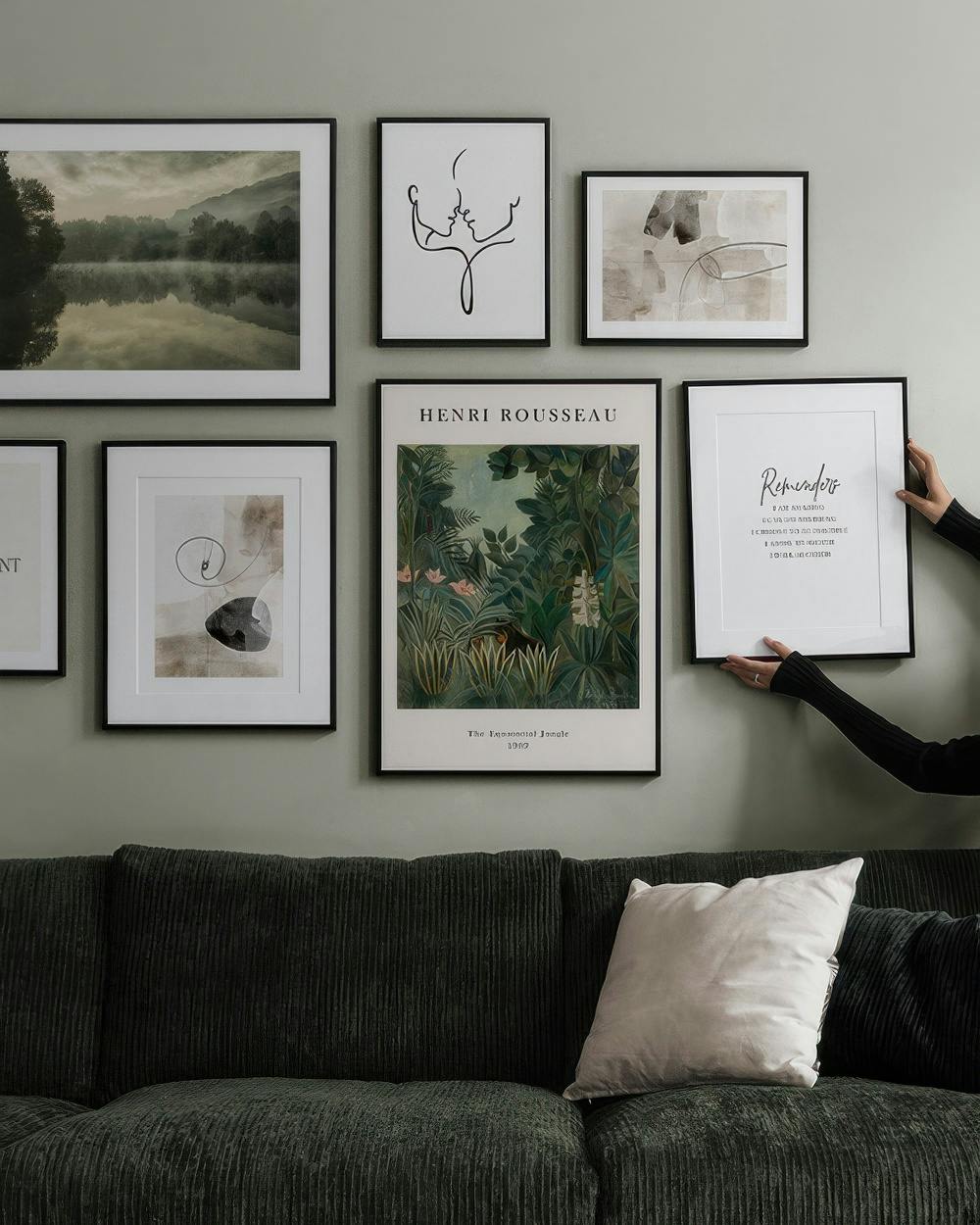 Eine Bilderwand mit verschiedenen Motiven über einem Sofa: Nebellandschaft, abstrakte Gesichter, Dschungel, organische Formen un