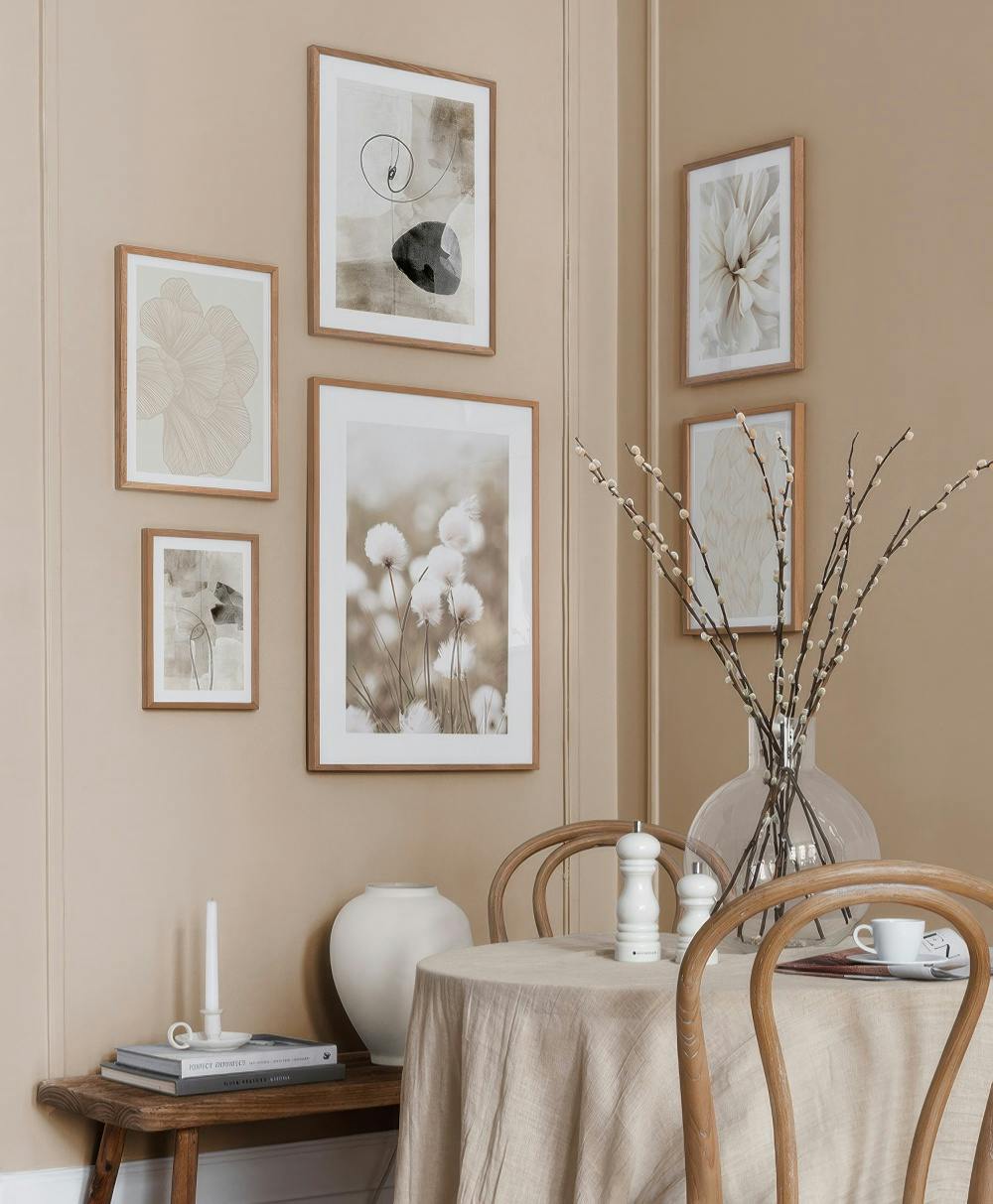 Eine Bilderwand mit abstrakten Drucken in Beige- und Brauntönen, einer Nahaufnahme von Baumwollgras und einer weißen Dahlie.