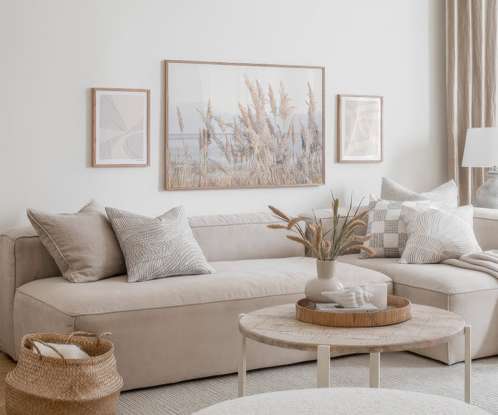 A gallery wall with a large landscape print of pampas grass by water and two smaller abstract prints in a neutral-toned living r