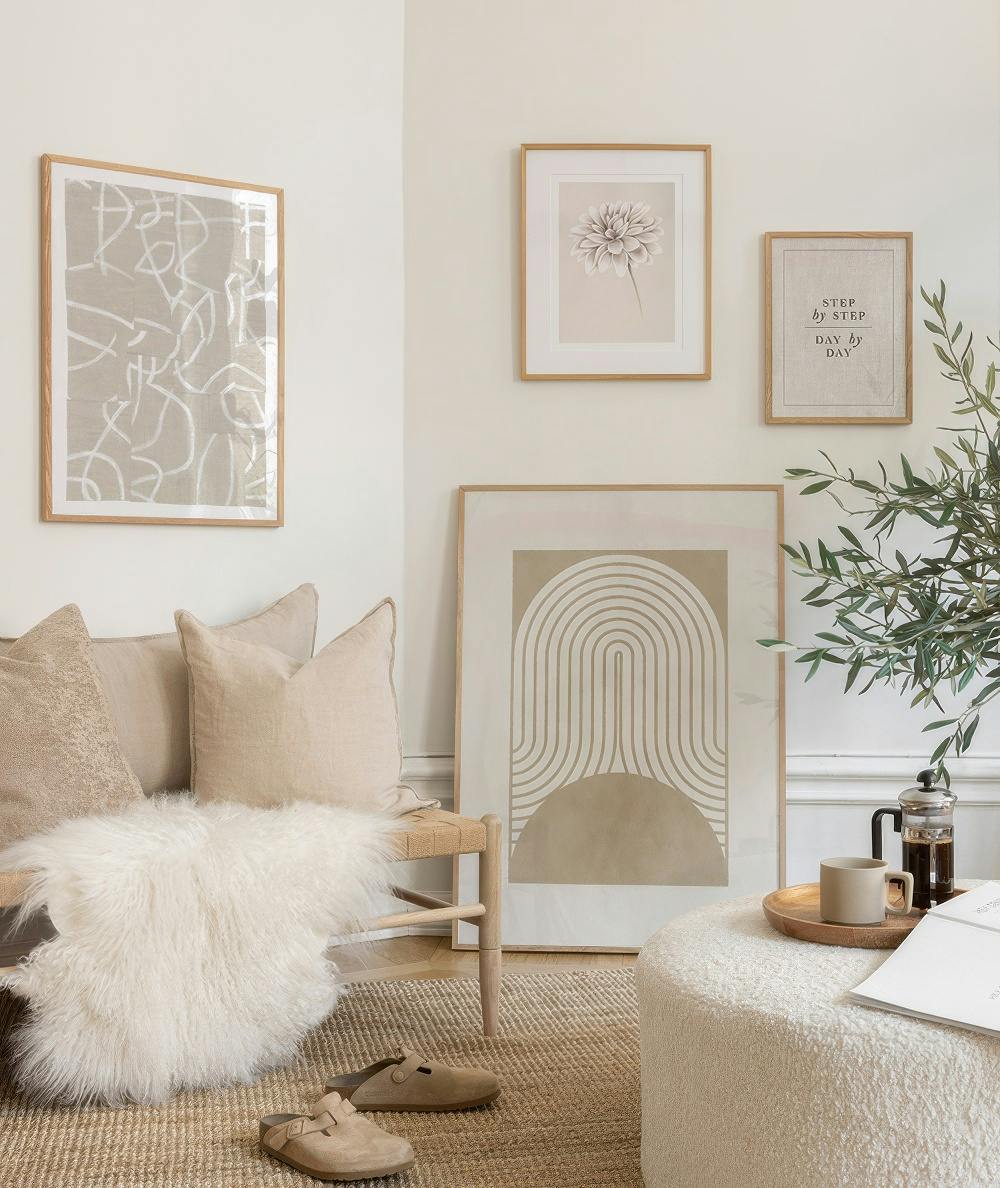 En tavelvägg i neutrala färger med fem tavlor i beige och vitt, föreställande abstrakt konst, en blomma och text.