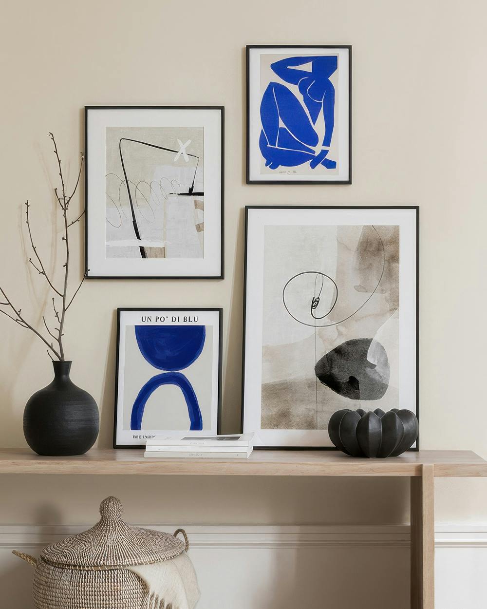 A gallery wall with four prints: a blue reclining figure, a black and white abstract swirl, a beige and black abstract line art,