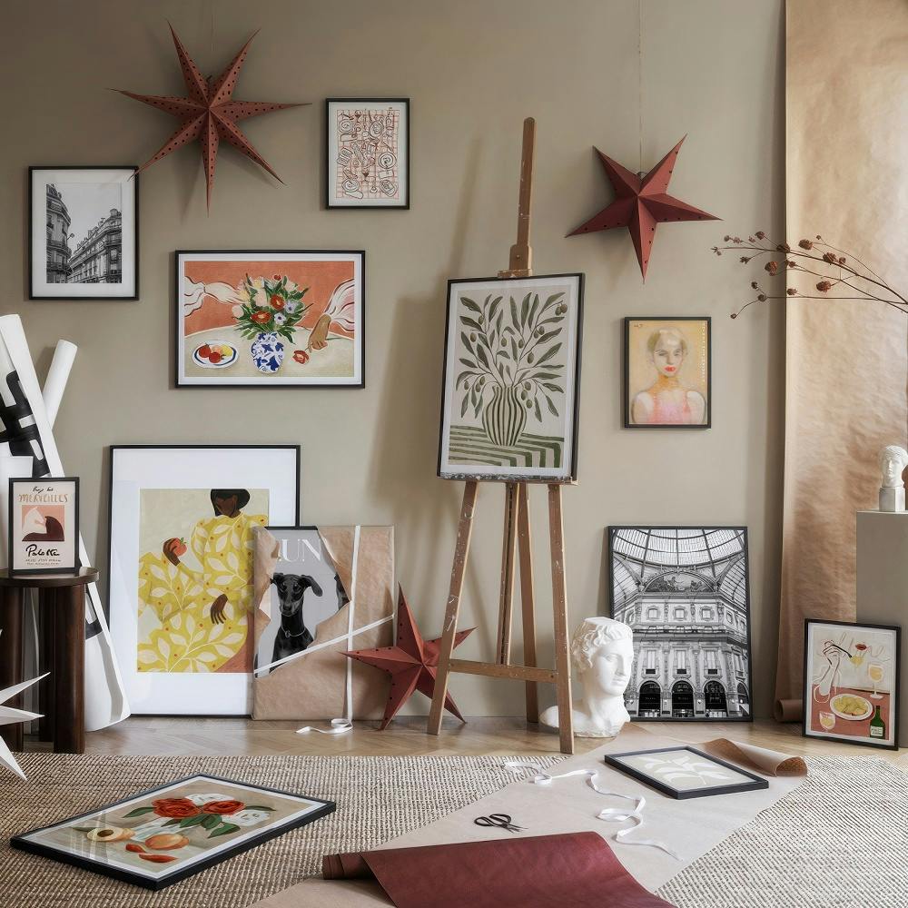 Décoration murale variée avec affiches, natures mortes et portraits, dans une pièce aux teintes terreuses.