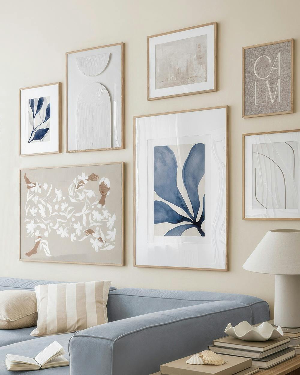 Eine Bilderwand über einem Sofa mit sieben gerahmten Bildern in Blau, Beige und Weiß, darunter abstrakte Blätter und florale Mus