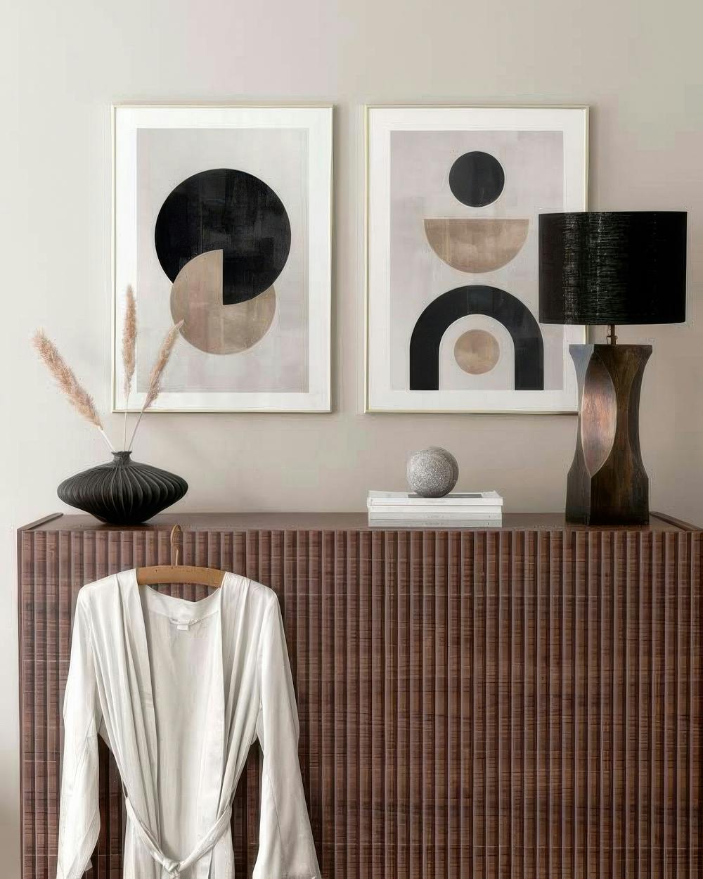 En tavelvägg med två abstrakta tavlor av geometriska former i svart och beige på en ljus bakgrund.