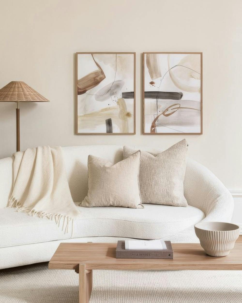 En tavelvägg med två abstrakta tavlor med organiska former i beige, brunt och grått över en vit soffa.