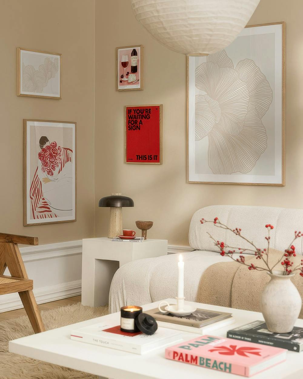 Una galleria a parete con stampe: una donna con rose rosse, un testo rosso THIS IS IT, vino e formaggio, e forme astratte beige.