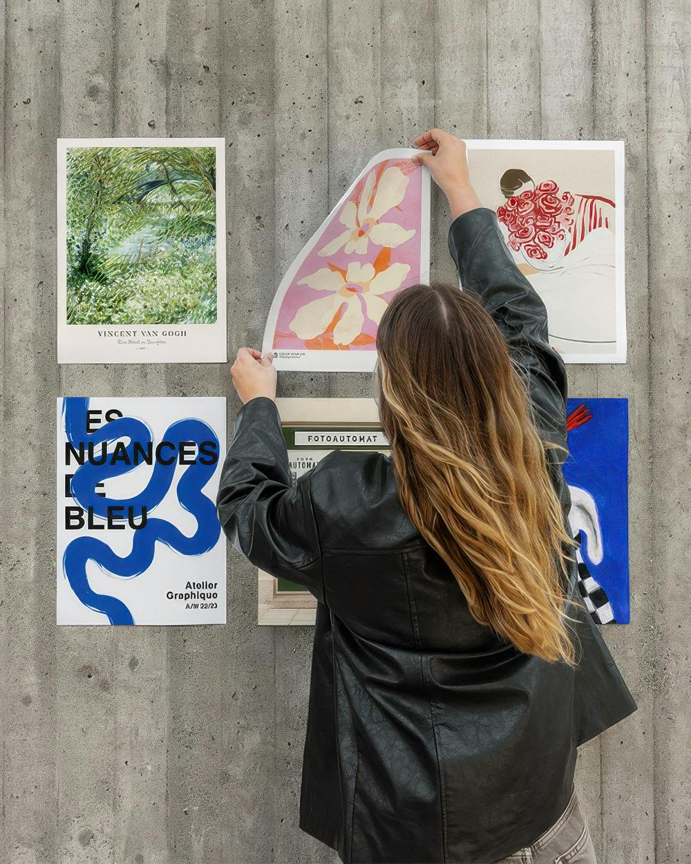 Une décoration murale avec une femme accrochant des affiches dart moderne, dont une de Van Gogh, sur un mur de béton.