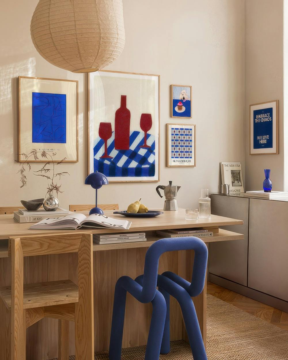 En tavelvägg med blå konst: abstrakt, vinflaska, tårta, text embrace the chaos och mönster i en matsal.