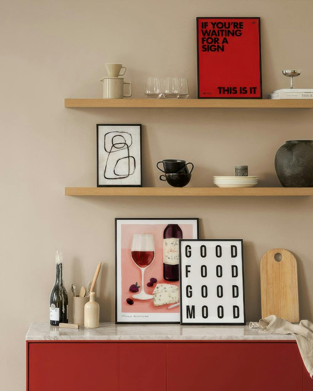 Eine Bilderwand mit einem roten Poster IF YOURE WAITING FOR A SIGN THIS IS IT, einem abstrakten Schwarz-Weiß-Bild und einem Wein
