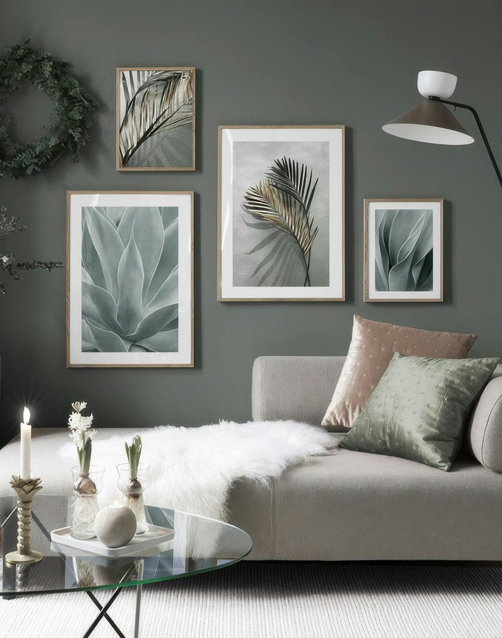 En tavelvägg med naturmotiv av palmblad i guld och grönt, samt agaveväxter, ovanför en soffa.