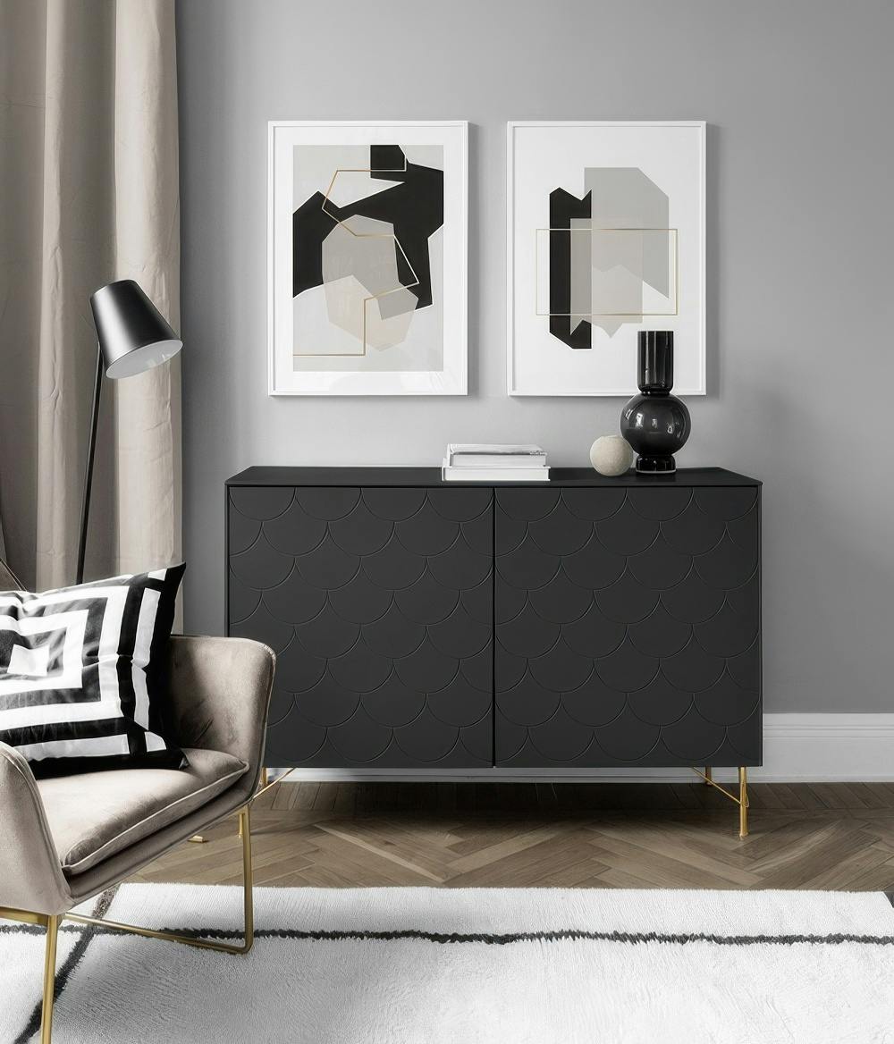 A gallery wall with two geometric prints featuring black, beige, and gold shapes on a light grey background, above a black cabin