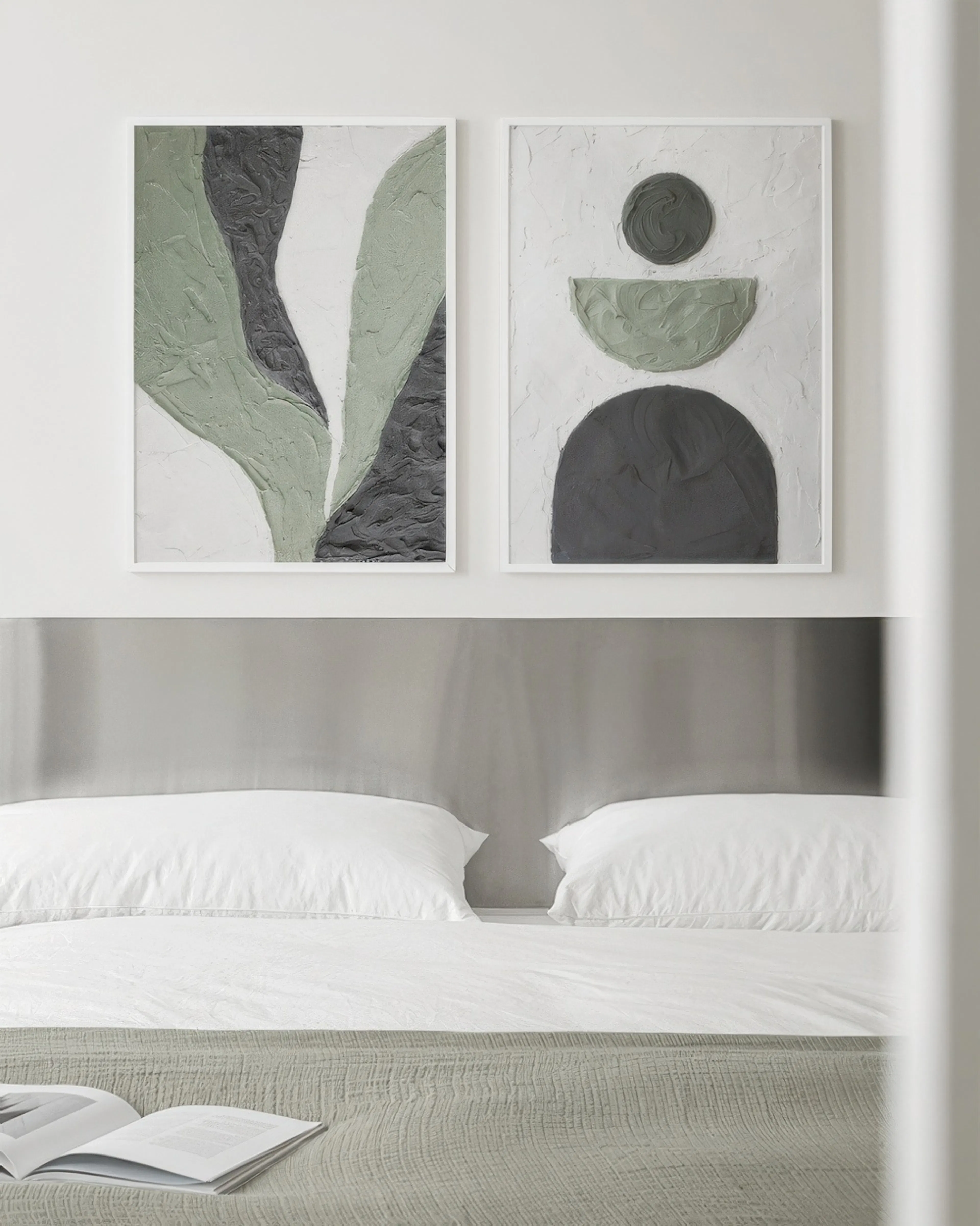 A poster pack featuring two abstract prints with sage green and dark grey textured shapes on a light background, above a bed.