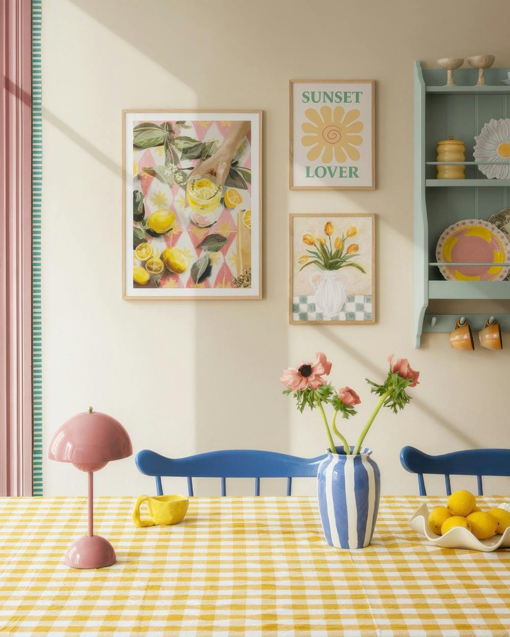 A poster pack featuring a lemon drink scene, a Sunset Lover graphic, and a vase of tulips, displayed on a cream wall above a yel