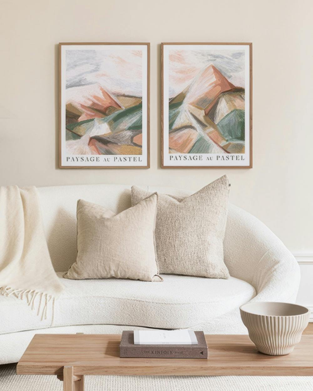 Dvojica abstraktných krajiniek v pastelových farbách s motívom hôr, zväzok plagátov visiacich nad bielym gaučom.
