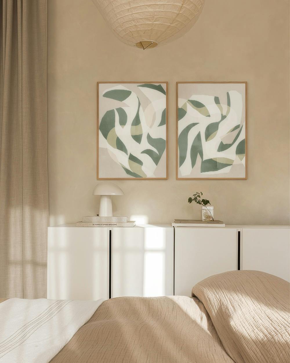 Twee postersets met abstracte groene en lichtbeige organische vormen aan een crèmekleurige muur.