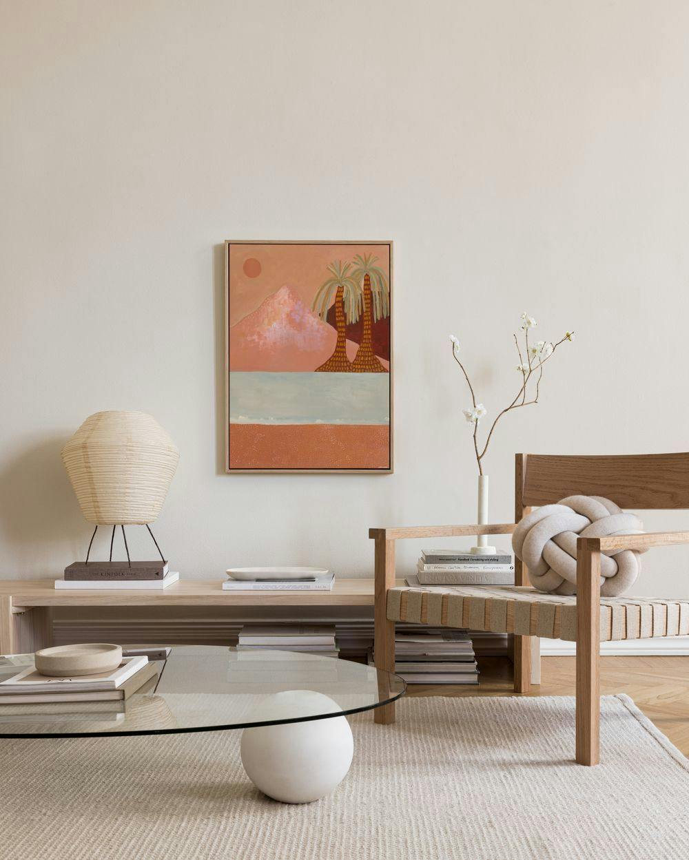 Toile murale désertique avec montagnes rosées, palmiers et un soleil orange au-dessus de locéan, suspendue dans un salon moderne