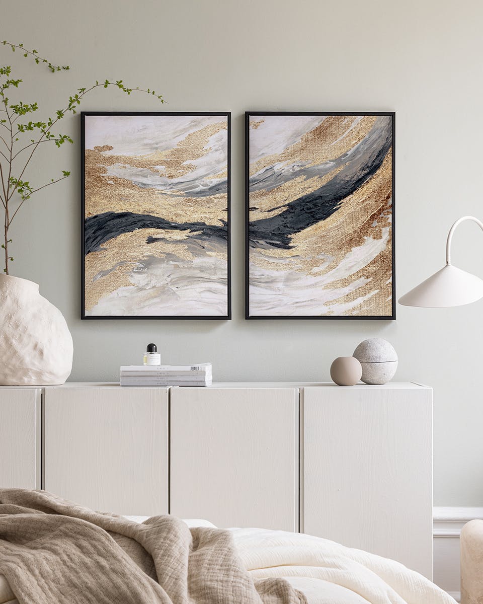 Posterset mit gold, schwarz, grau und weiß geschwungenen Mustern, über einem Sideboard in einem Schlafzimmer.