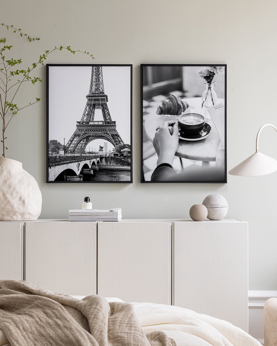 A poster pack featuring two black and white Paris-themed prints, displayed above a white cabinet in a bedroom.