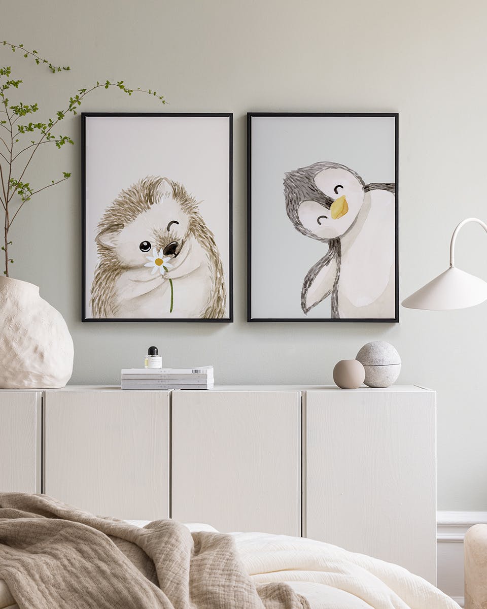 Dva plakáty se zvířaty v dětském pokoji. Ježek s kopretinou a tučňák, visící nad bílou komodou.