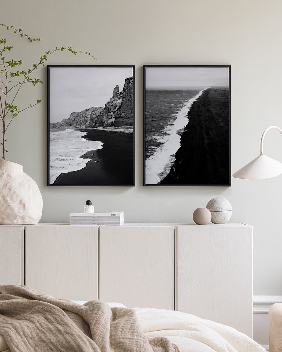 Posterset mit zwei Schwarz-Weiß-Postern von Küstenlandschaften über einem Schrank in einem Schlafzimmer.