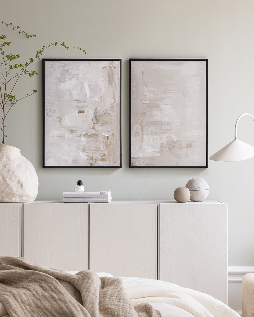 Lot de posters abstraits aux tons beiges et blancs, affichés sur un meuble clair dans une chambre.