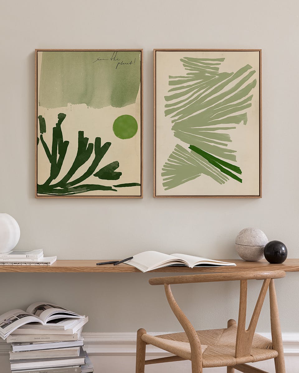 Two abstract green prints with organic shapes and lines, hanging above a wooden desk with books in a home office.
