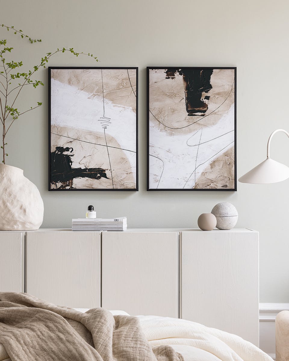 Zestaw plakatów z abstrakcyjnymi wzorami w odcieniach beżu, bieli i czerni, zawieszony nad białą komodą w sypialni.