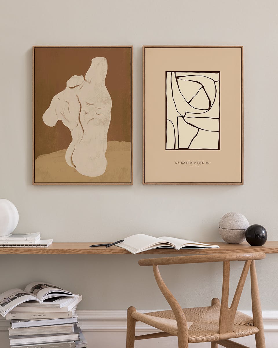 A gallery wall with two poster packs: a beige abstract figure on brown, and a light beige geometric design, above a wooden desk