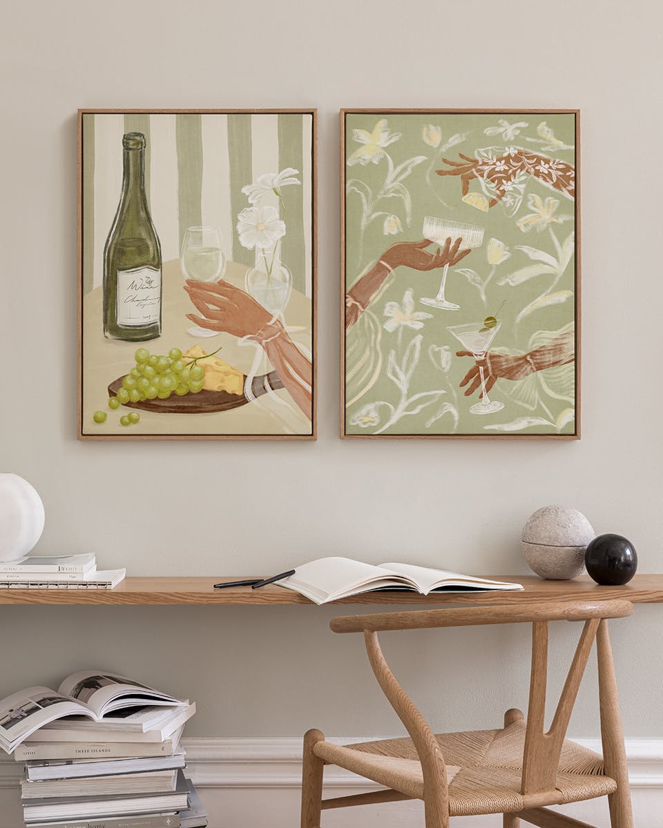 Due poster con illustrazioni di bevande e mani in stile bohémien, appesi sopra una mensola in legno con libri e oggetti decorati