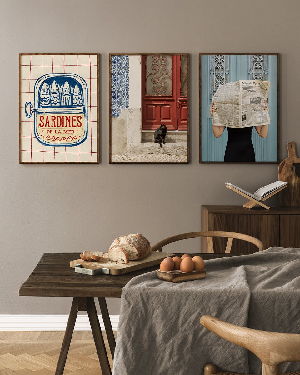 Postersets met o.a. sardineblik, zwarte kat bij rode deur en vrouw met krant, hangend boven een houten tafel.