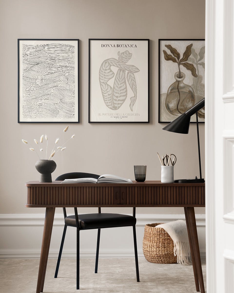 A gallery wall of three framed posters, including abstract waves, a seated figure, and a botanical vase, displayed above a woode