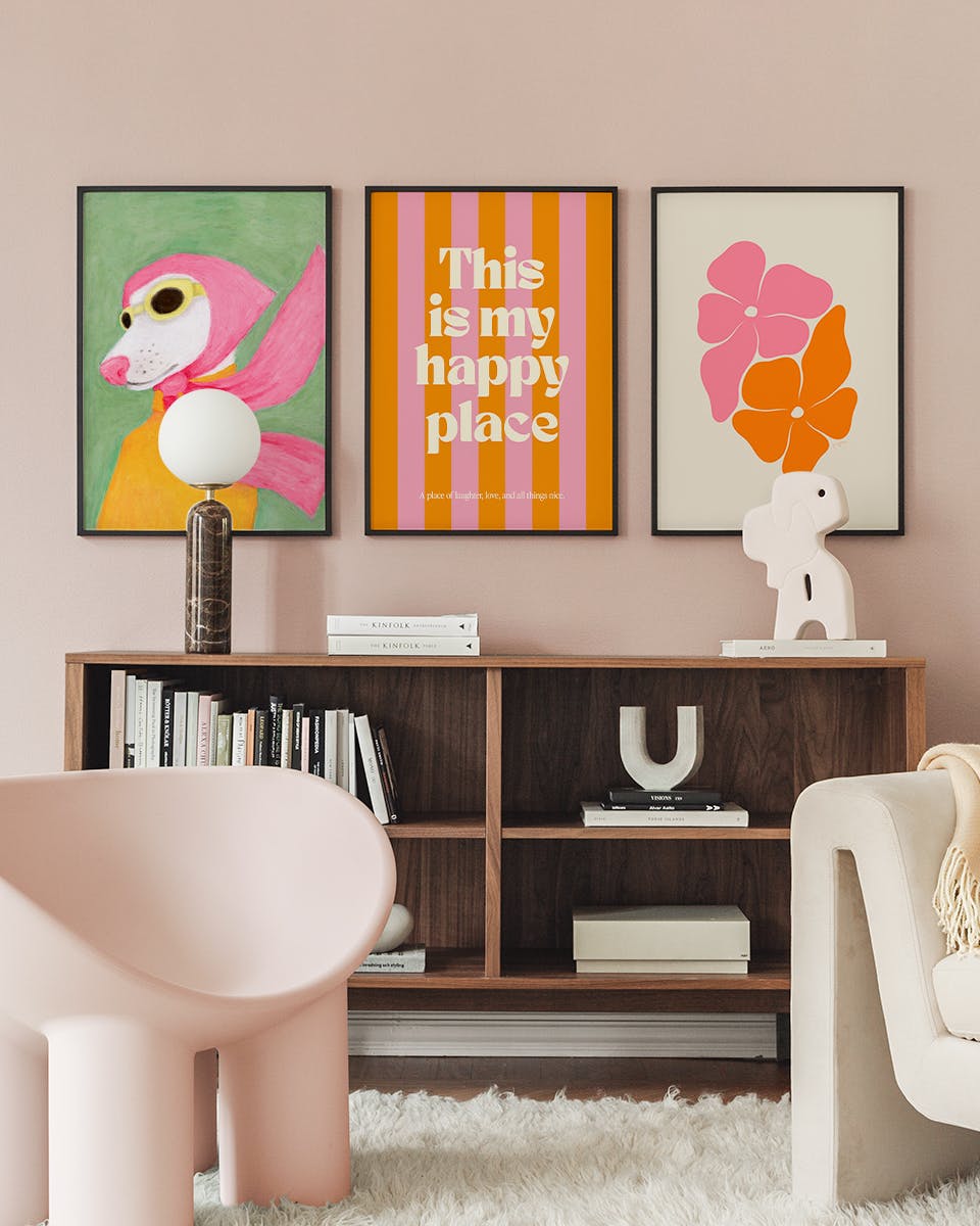 Paquetes de pósters exhibidos en una sala rosa con un mueble de madera, una silla rosa y una alfombra.