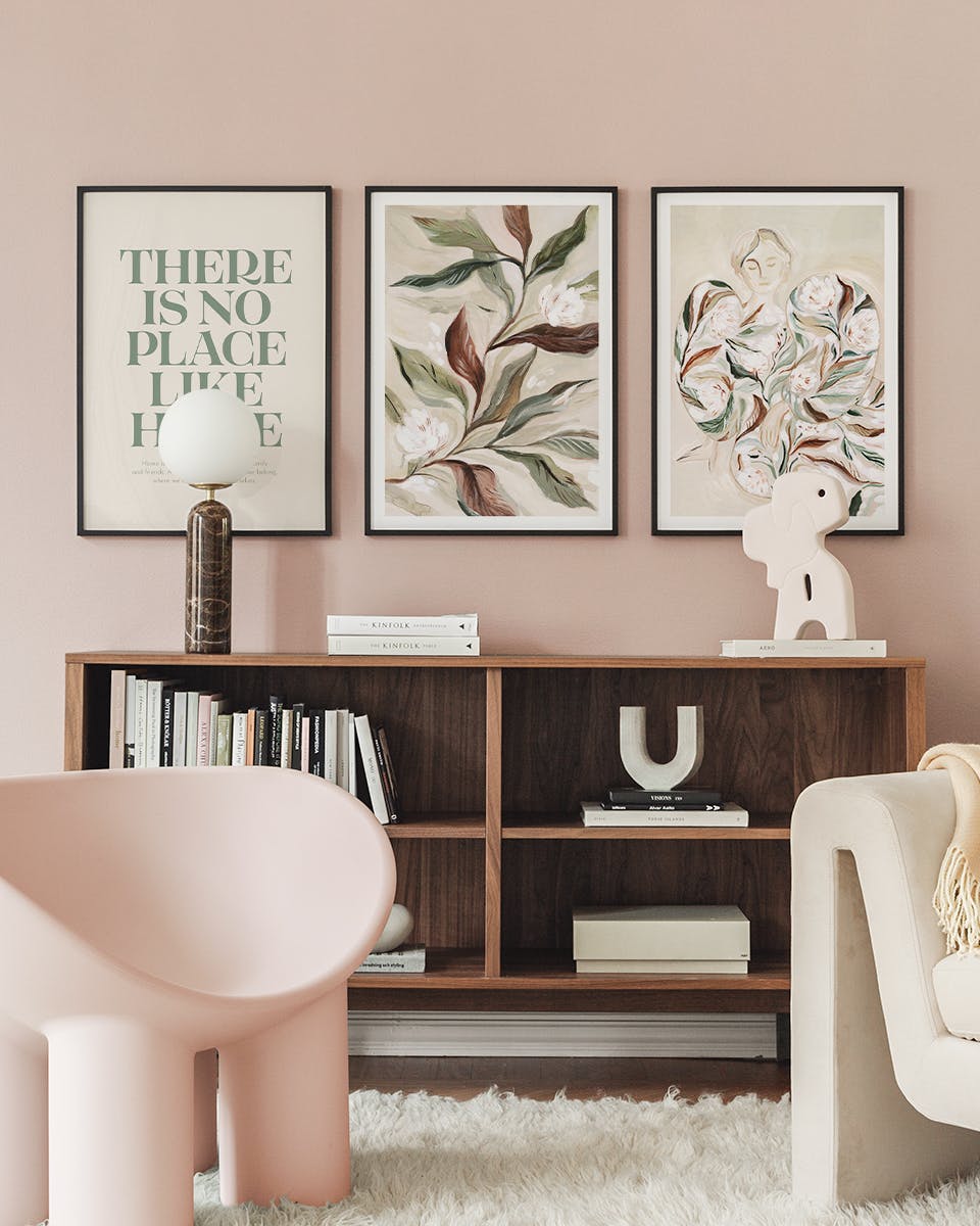 En plakatpakke med tre grønne og beige plakater, der hænger over en træskænk i en moderne stue med lyserøde vægge.