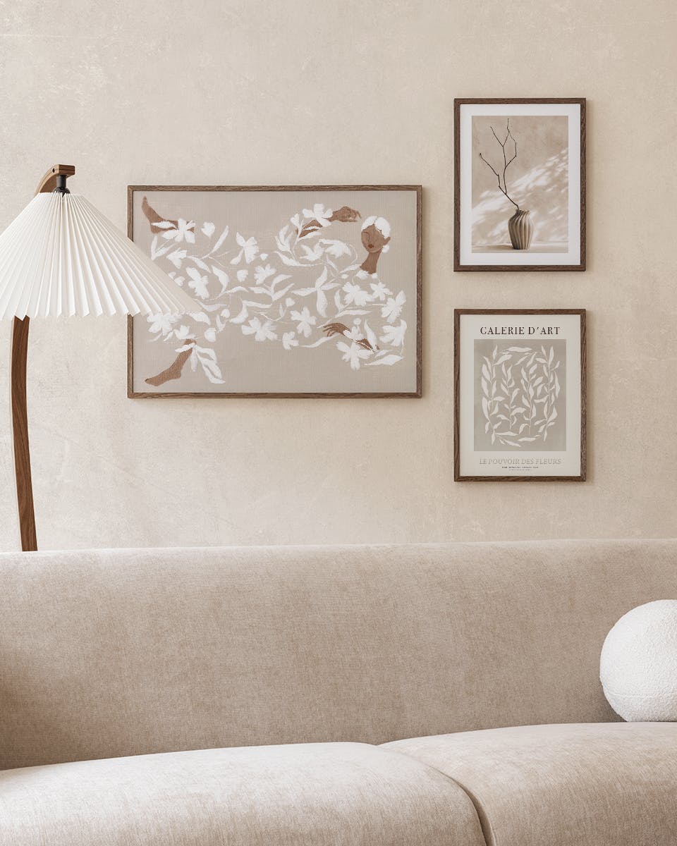 Tres paquetes de pósters exhibidos sobre un sofá beige en una sala de estar moderna, con una lámpara de pie.