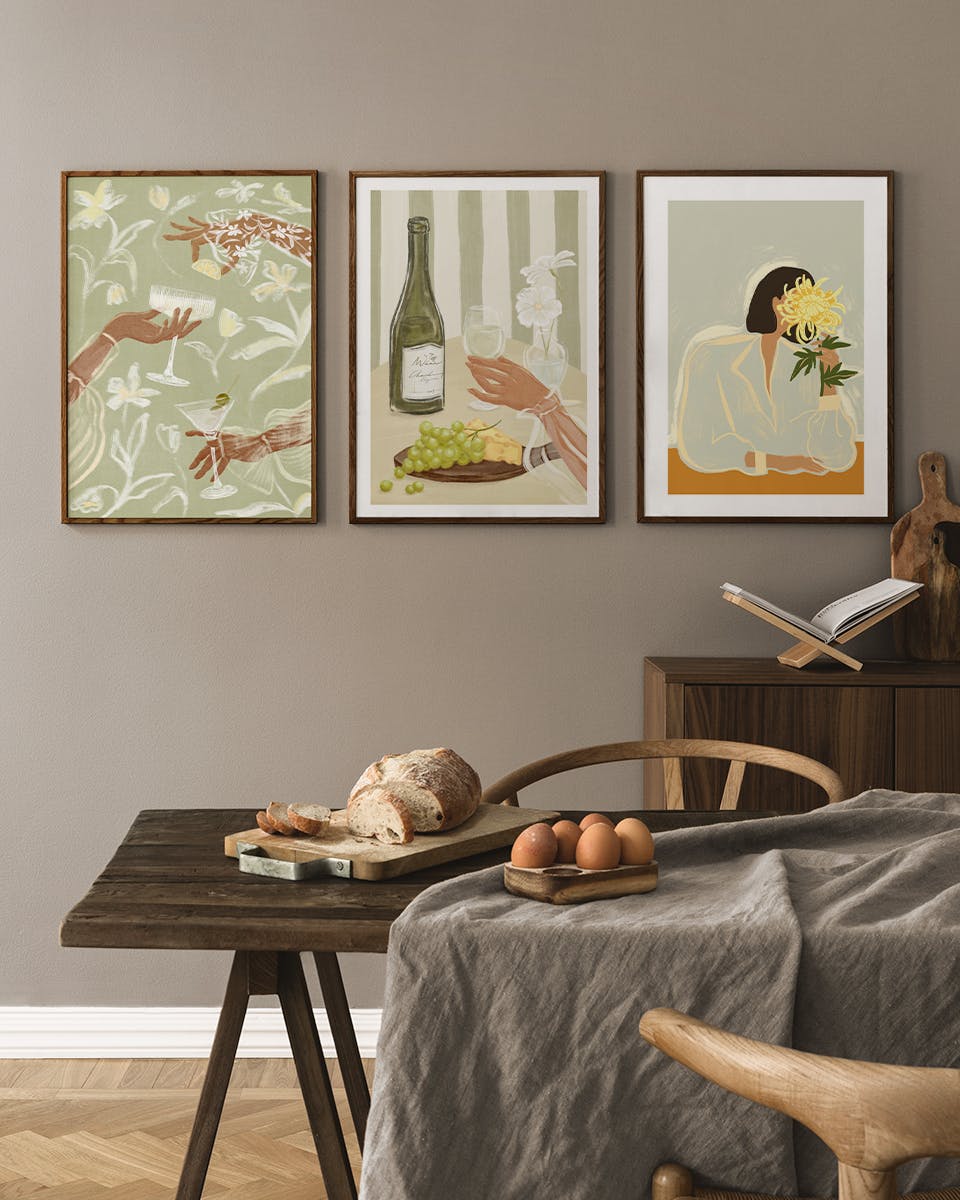 Tre affischer i ett posterpaket med illustrationer av händer, dryck, mat och en kvinna med blommor, hängande i ett kök.