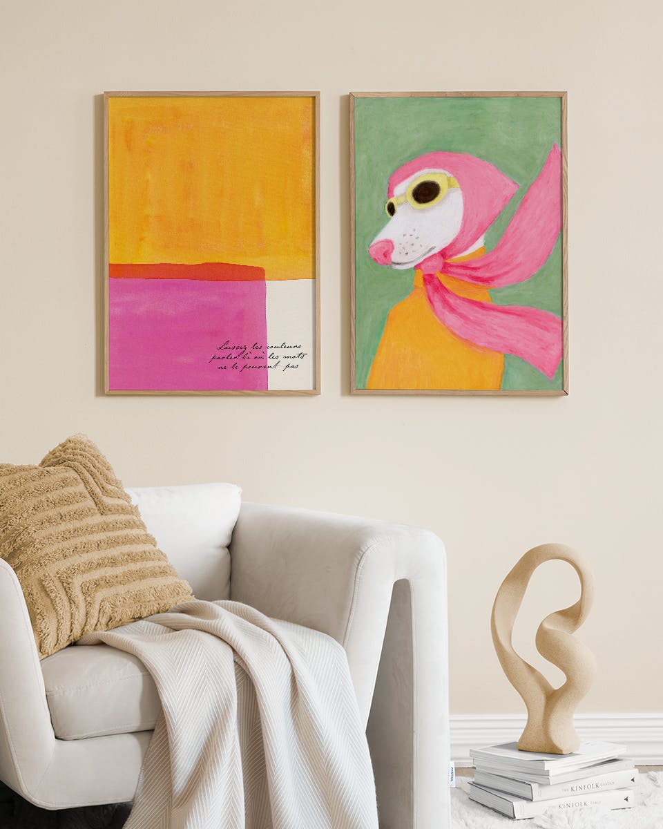 Dwa plakaty zawieszone nad beżową sofą. Jeden to abstrakcja z żółtymi i różowymi pasami, drugi przedstawia psa w różowej chuście