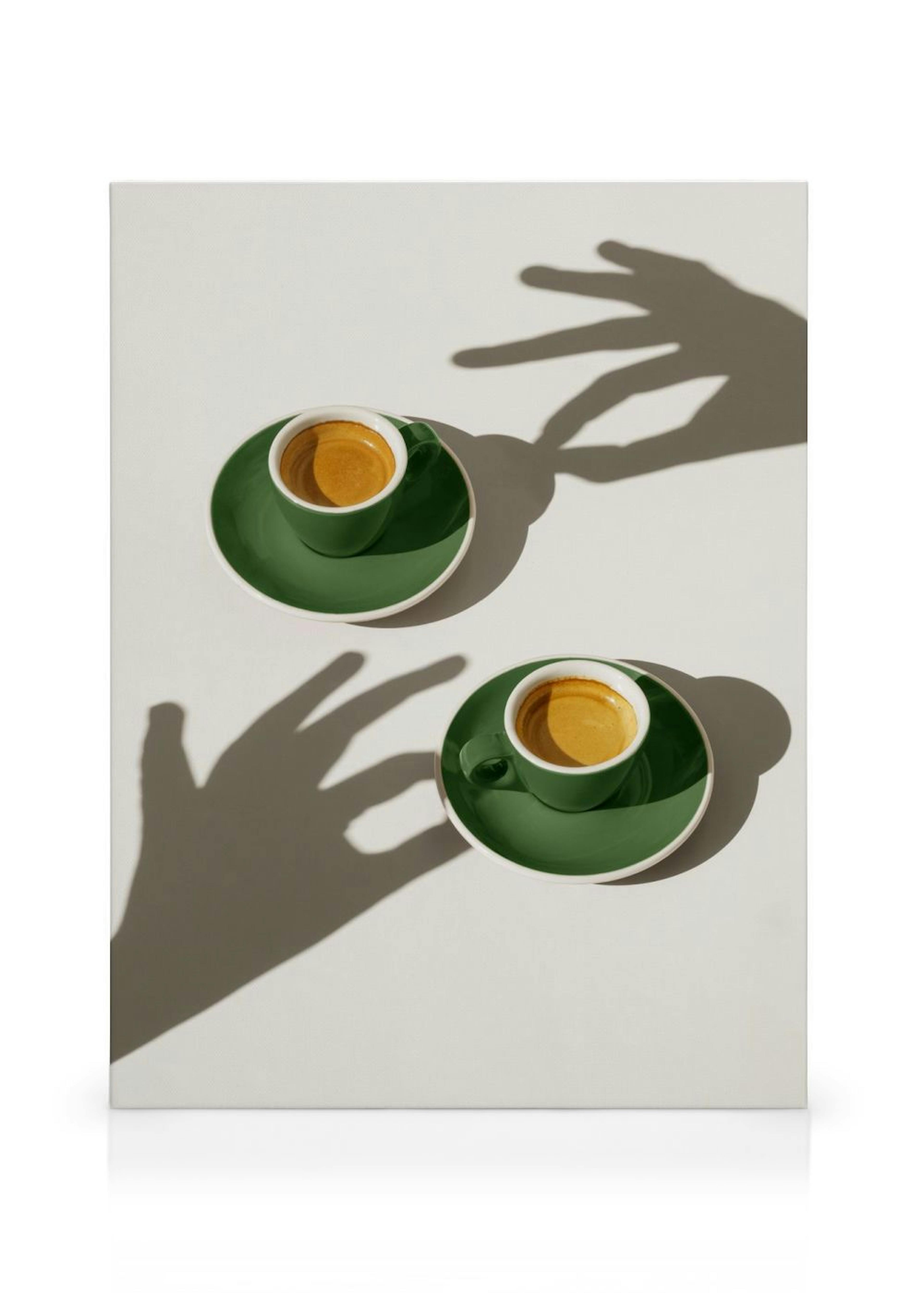 Leinwandbild mit zwei grünen Espressotassen und Untertassen auf hellem Hintergrund, beleuchtet von Schatten spielender Hände.