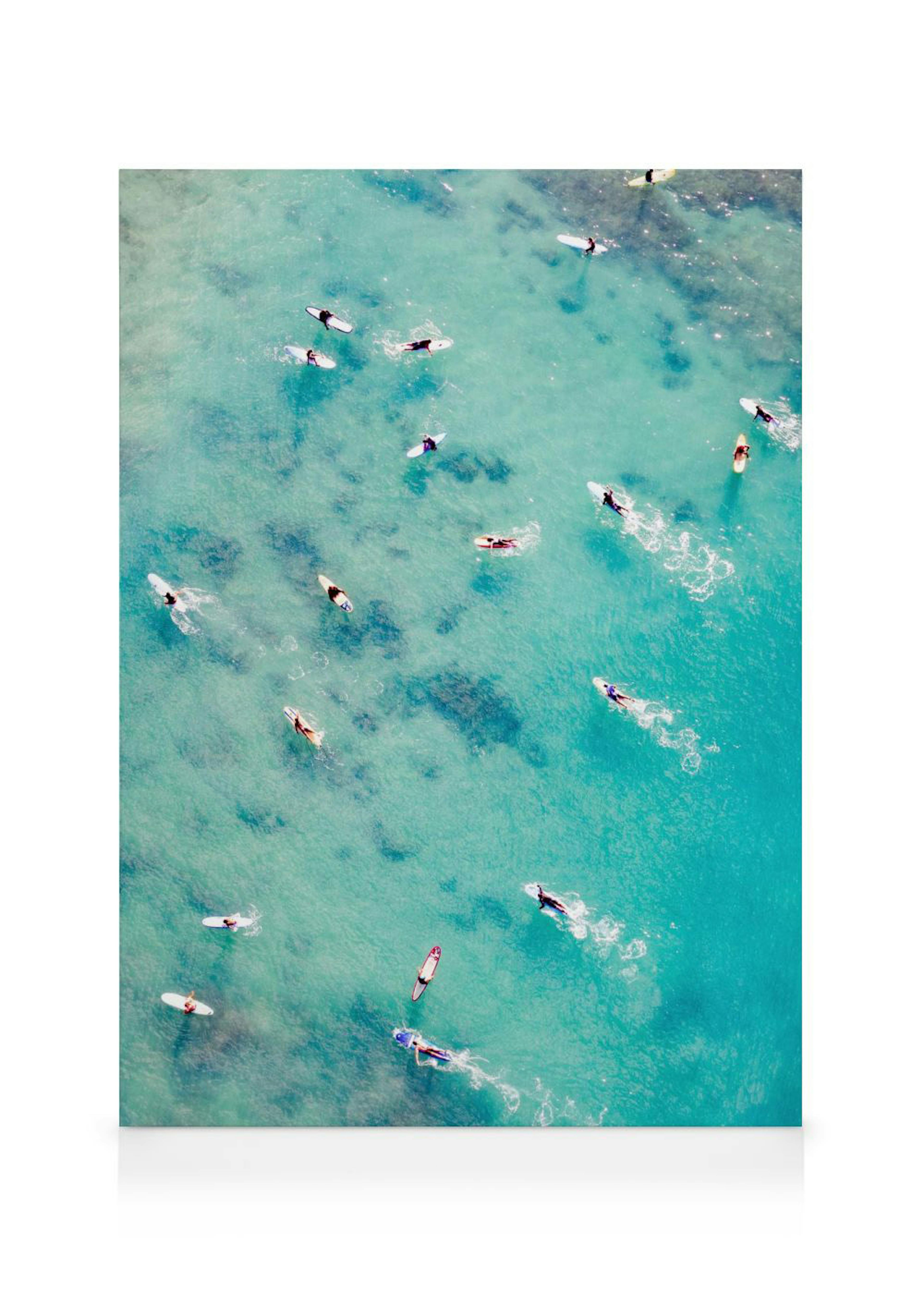 Leinwandbild mit einer Luftaufnahme von Surfern und ihren Surfbrettern auf türkisblauem Wasser.