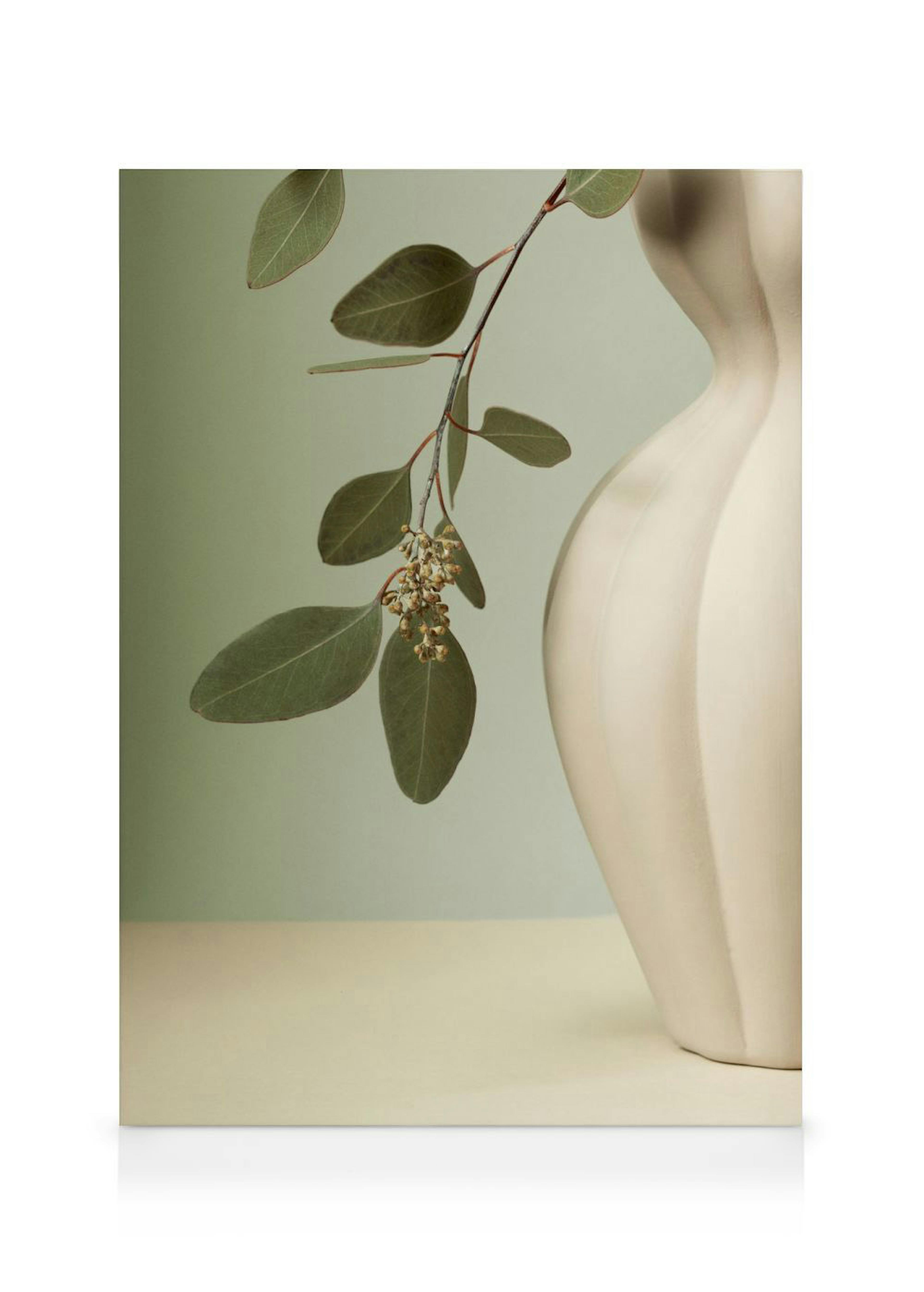 Toile murale avec une branche deucalyptus aux feuilles vertes et petites fleurs, à côté dun vase crème texturé.
