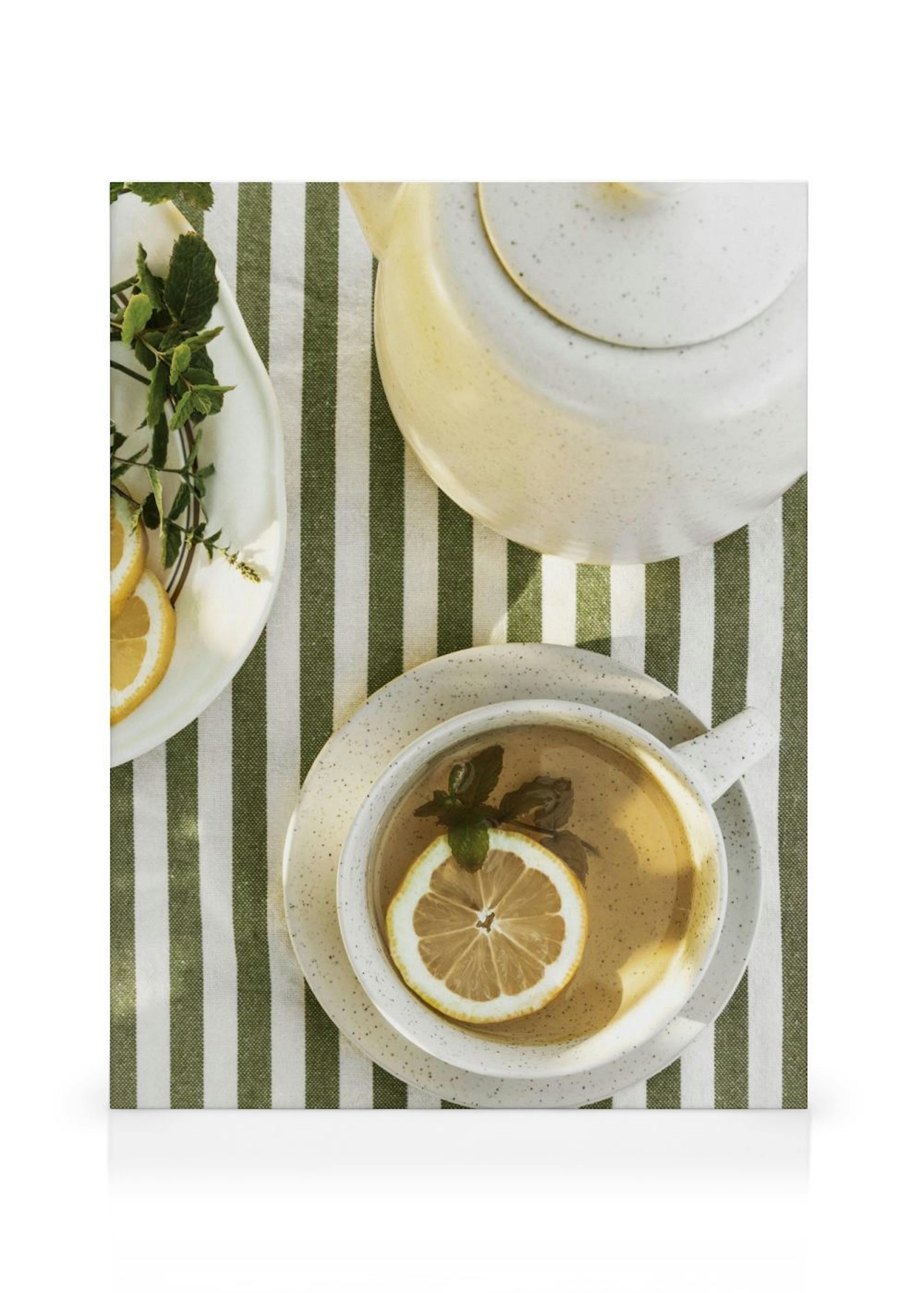 Leinwandbild einer Tasse Tee mit Zitrone und Minze, Teekanne und Zitronenscheiben auf gestreiftem Tuch.