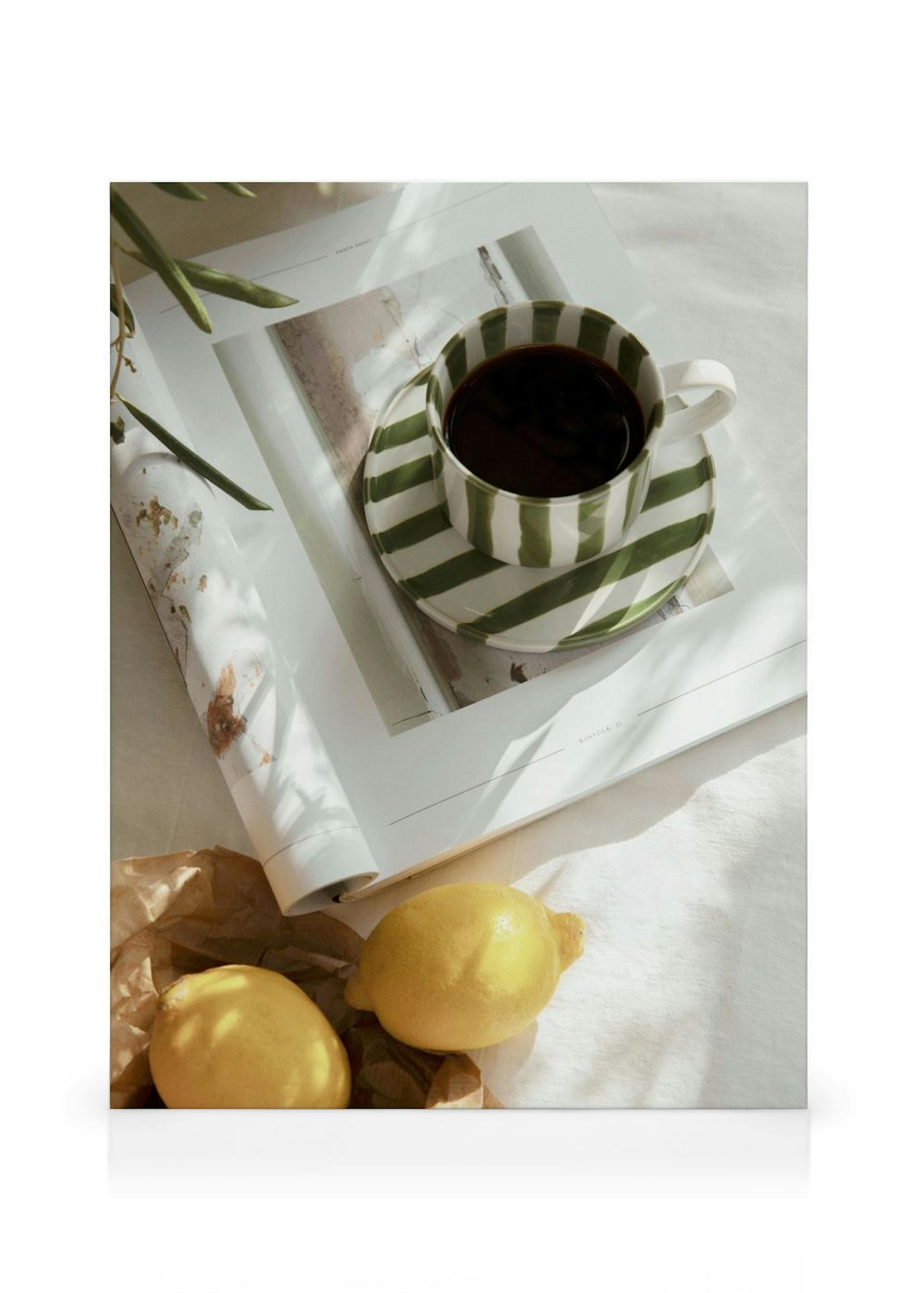 Leinwandbild mit Kaffeetasse, Untertasse, Magazin und Zitronen auf hellem Stoff, in einem gemütlichen Raum.