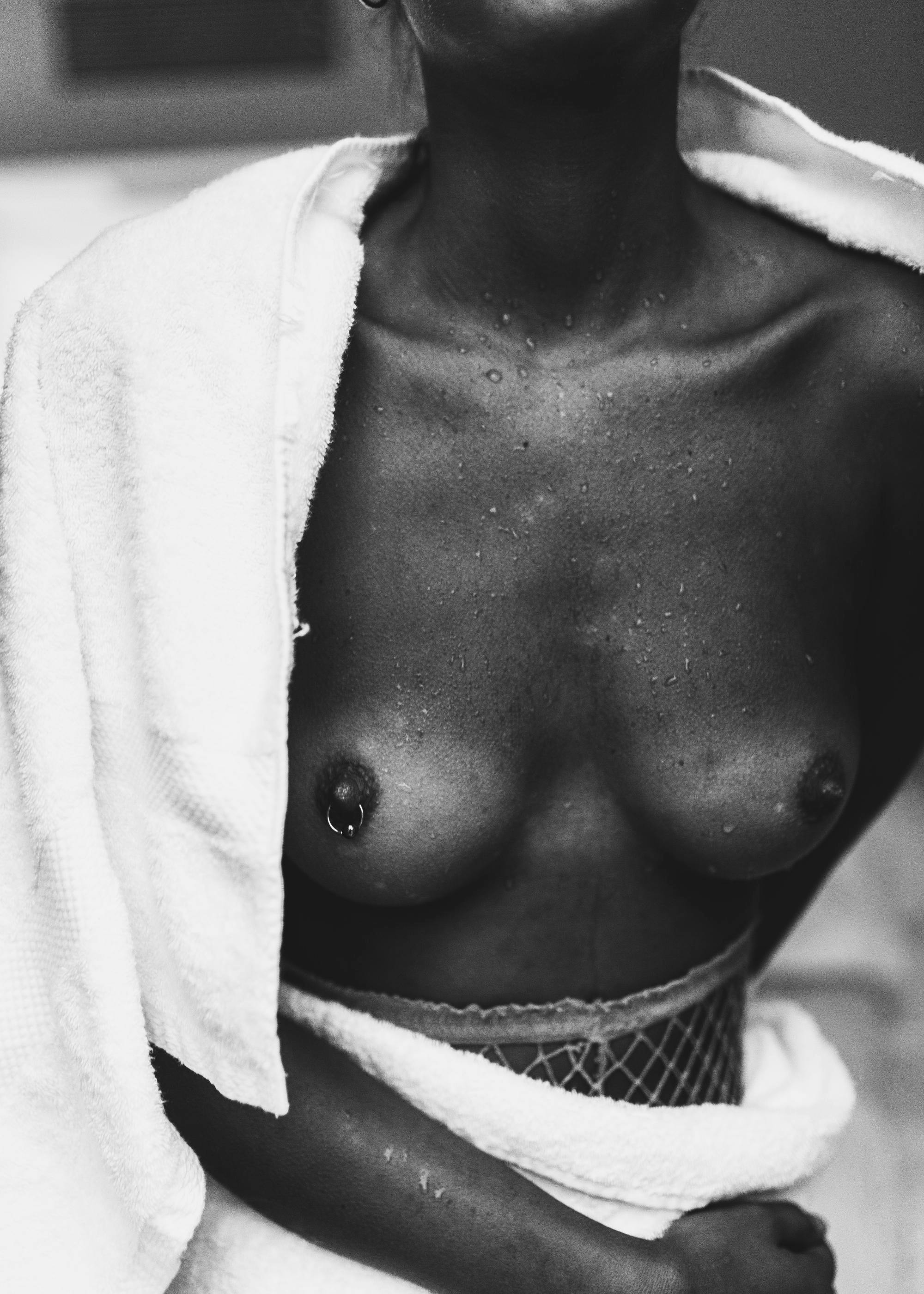 Schwarz-Weiß-Fotografie einer nassen Brust, ein Handtuch über der Schulter, Piercing