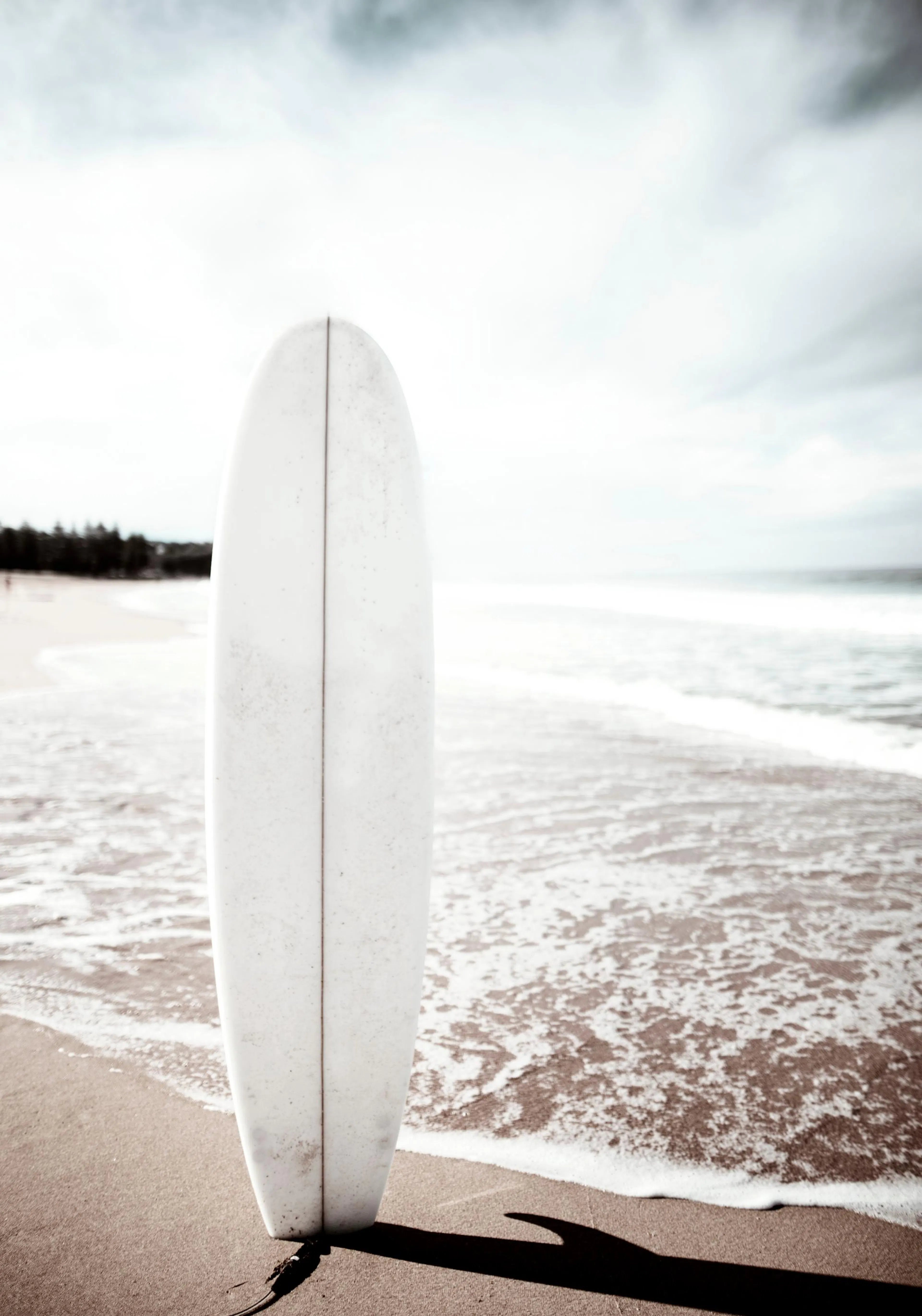 Bílý surf na písčité pláži s mořskými vlnami v pozadí, fotografie léta u oceánu.