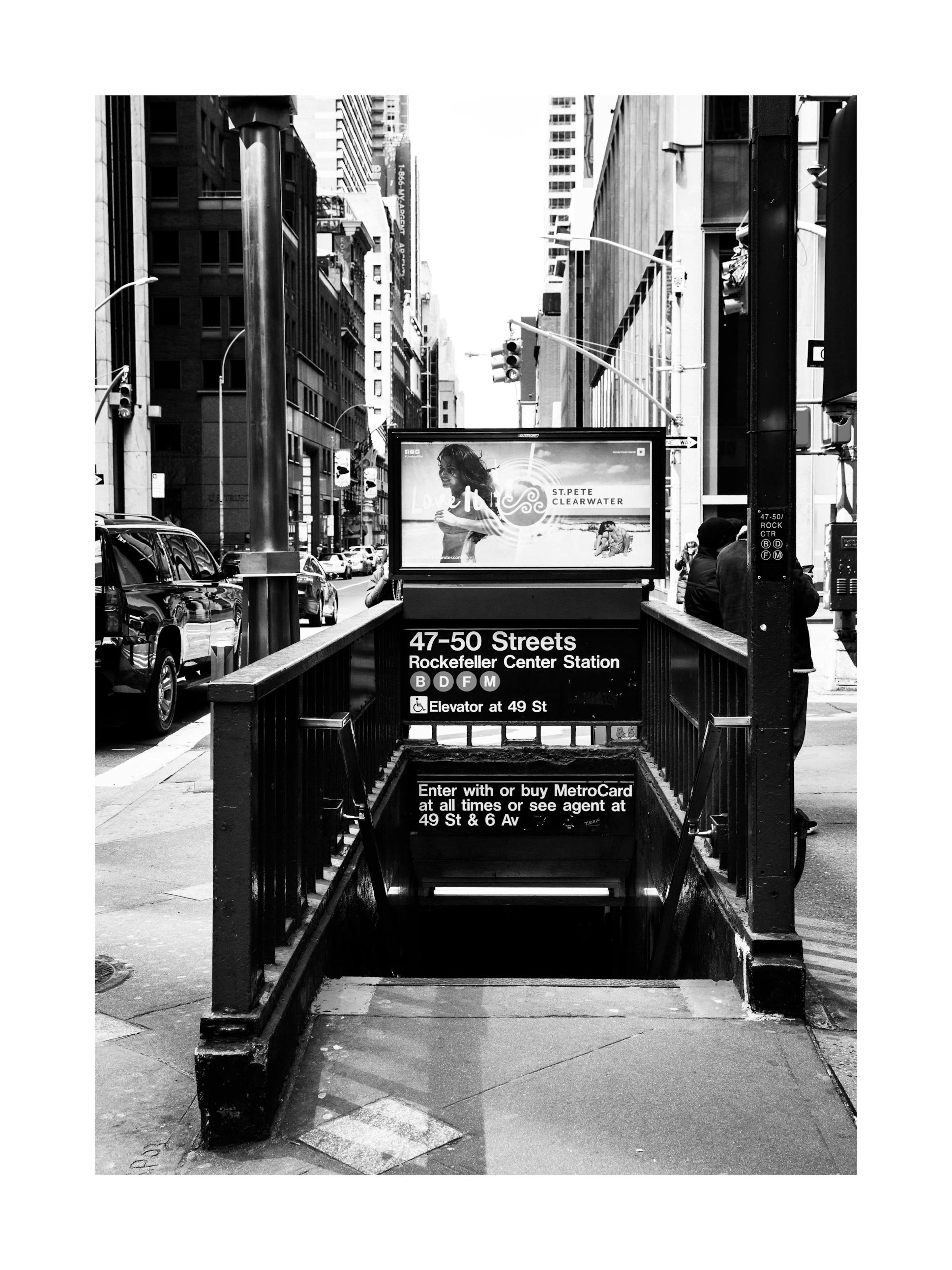 Schwarz-Weiß-Poster: Eingang zur New Yorker U-Bahn-Station Rockefeller Center mit Schildern und Straßenbild.