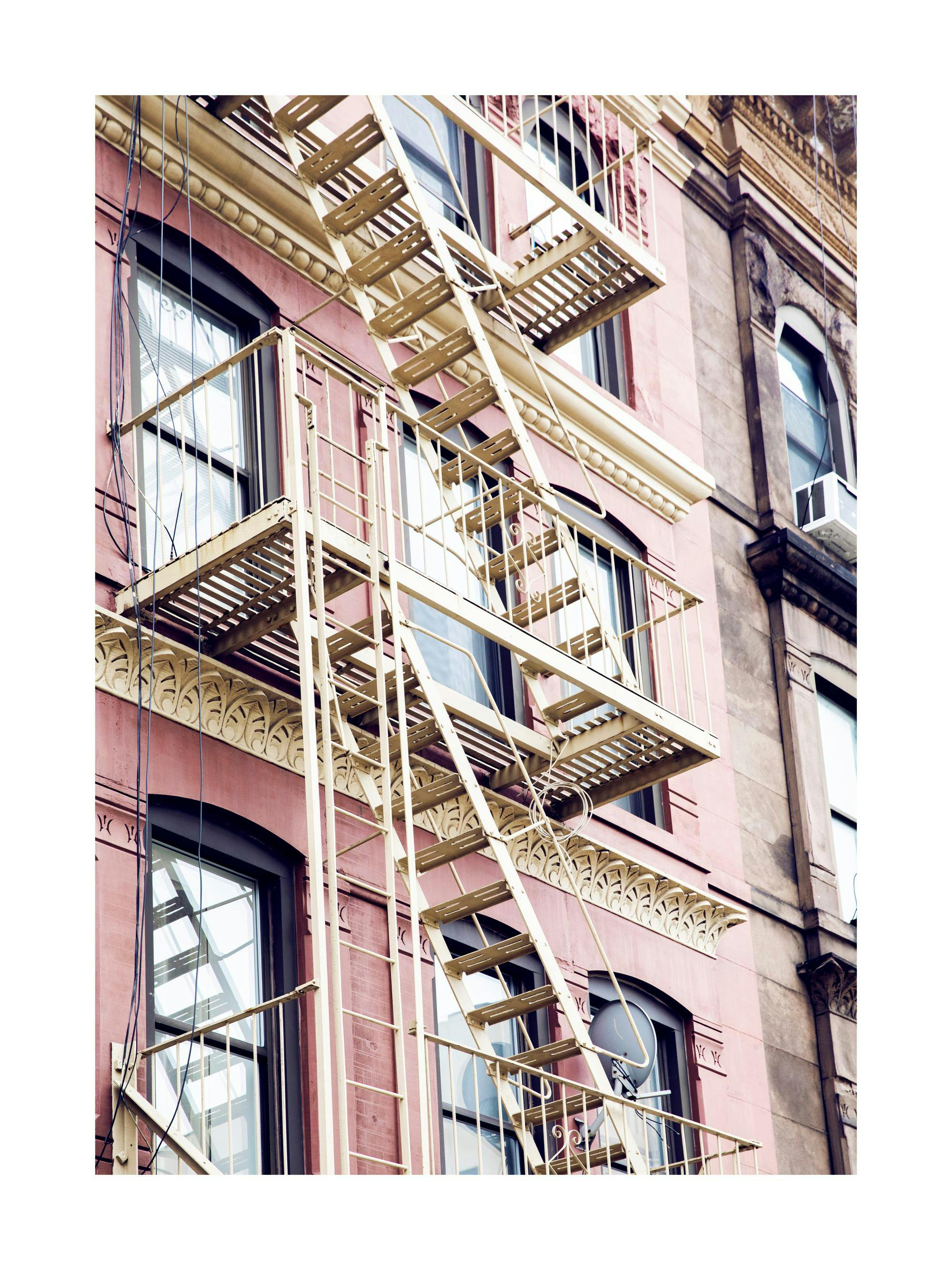 New Yorks brandtrappor på en rosa byggnad i tegel, med detaljerade fönster och balkonger som ger urban charm.