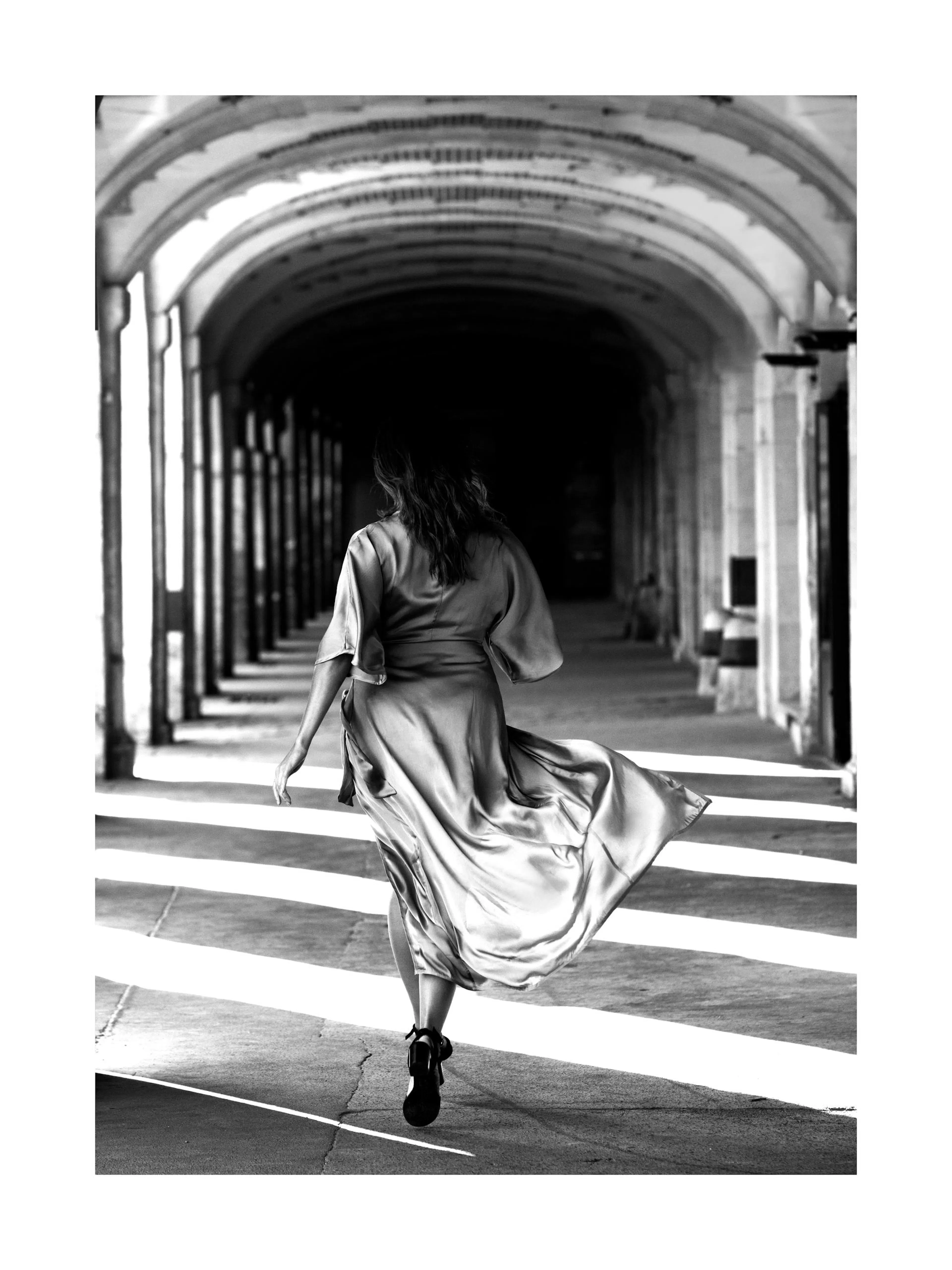 Svartvit fotokonst av kvinna i sidenklänning som springer genom en valvkorridor i Paris, fashion design.