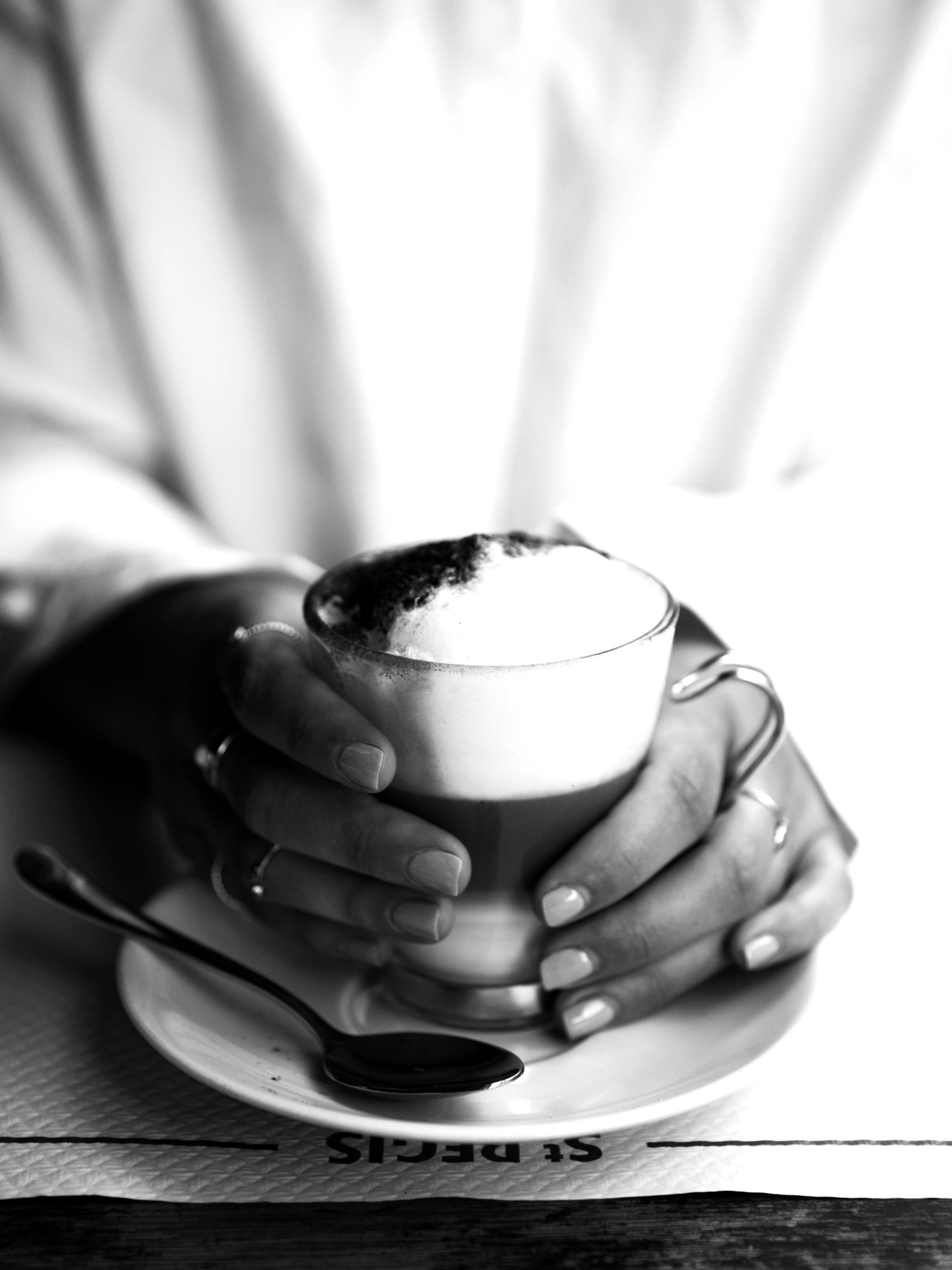 Affiche noir et blanc de mains tenant une tasse de café au lait mousseux, style typographie St Regis