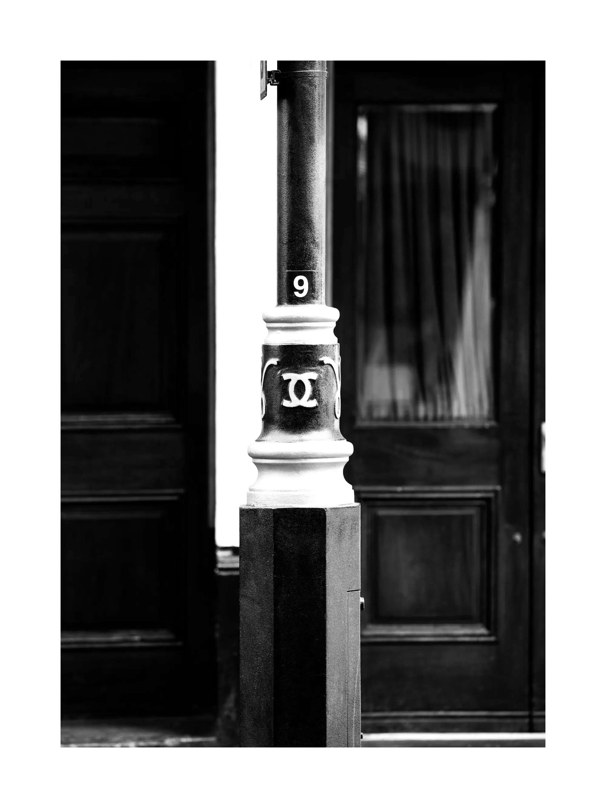 Black and white fashion print of a lamppost with the Chanel logo and number 9 on a street poster.