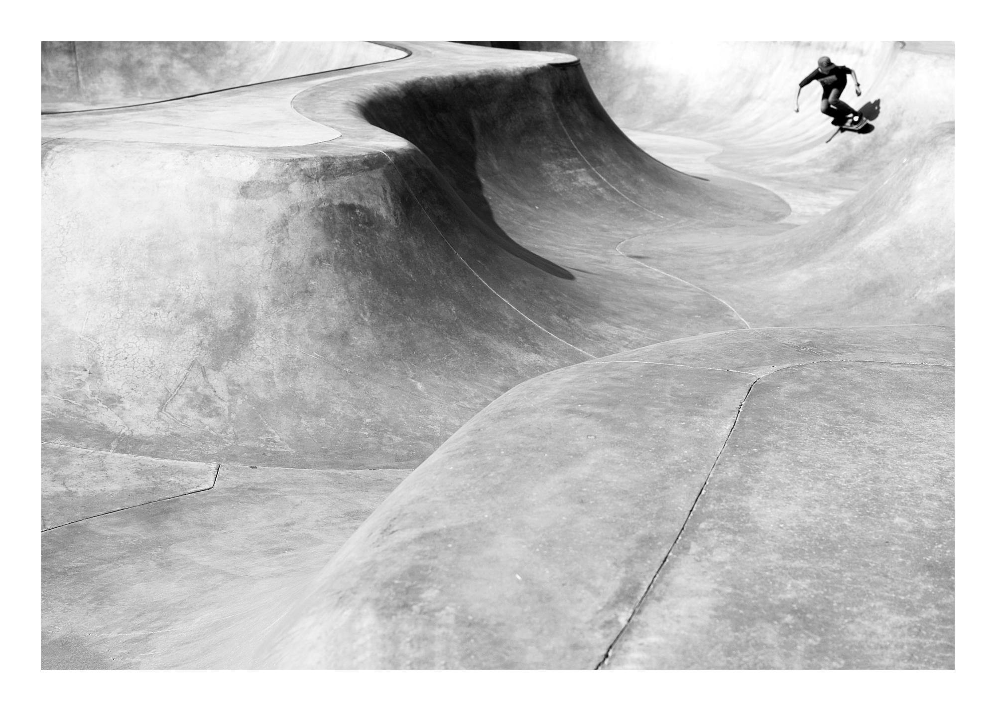 Zwart-wit poster van een skateboarder die hoog in de lucht springt in een skatepark met betonnen golven.